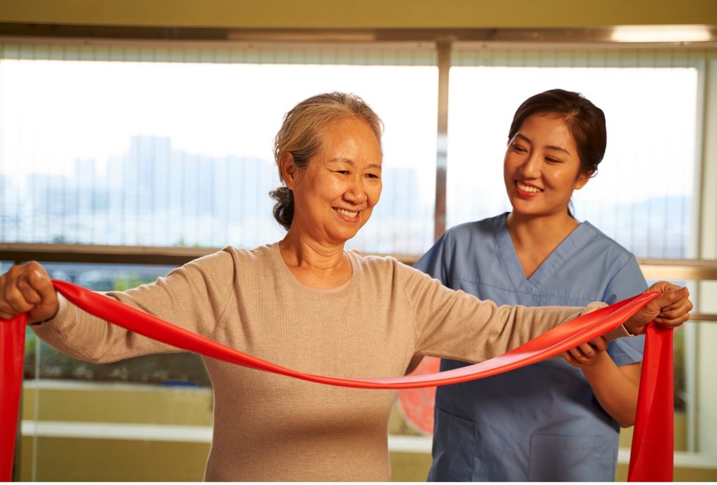 Therapist assisting senior patient with resistance band rehabilitation exercise